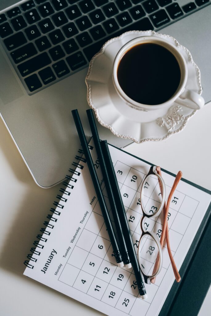 Flat lay of a coffee cup, calendar, and laptop for a productive workspace setup.